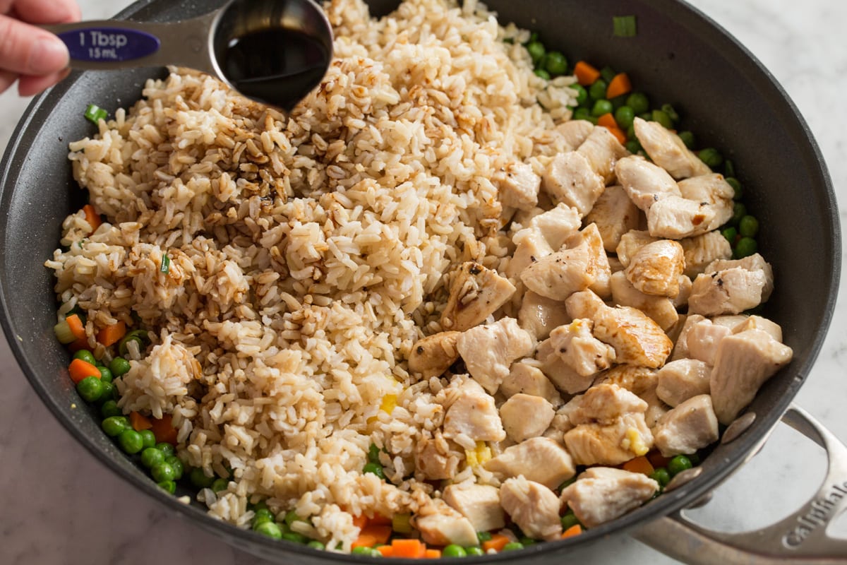 Chicken Fried Rice Pouring soy sauce over brown rice and chicken pieces in a large skillet to finish fried rice.
