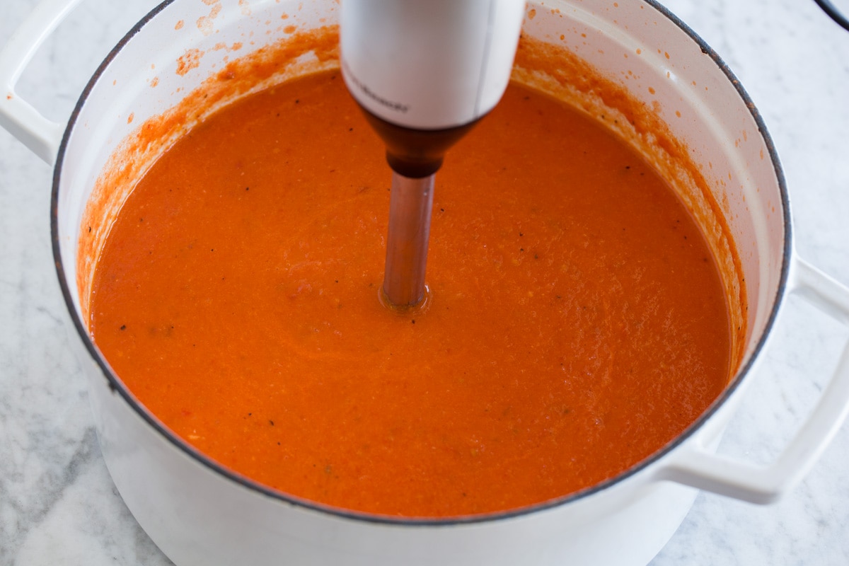 Roasted Tomato Basil Soup Roasted tomato basil soup being blended in a pot with an immersion blender.