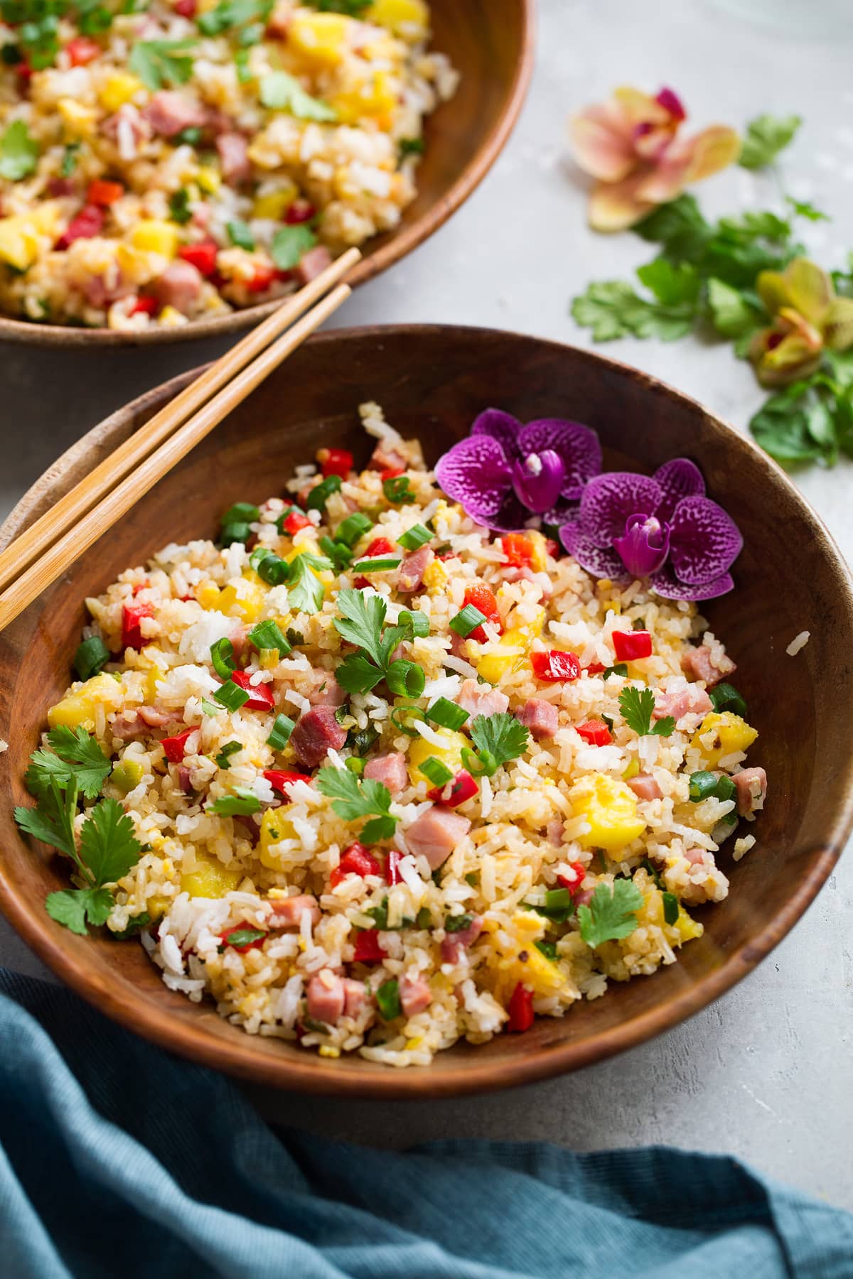 Hawaiian Fried Rice Wooden bowl full of hawaiian fried rice decorated with flowers and chopsticks to the side.