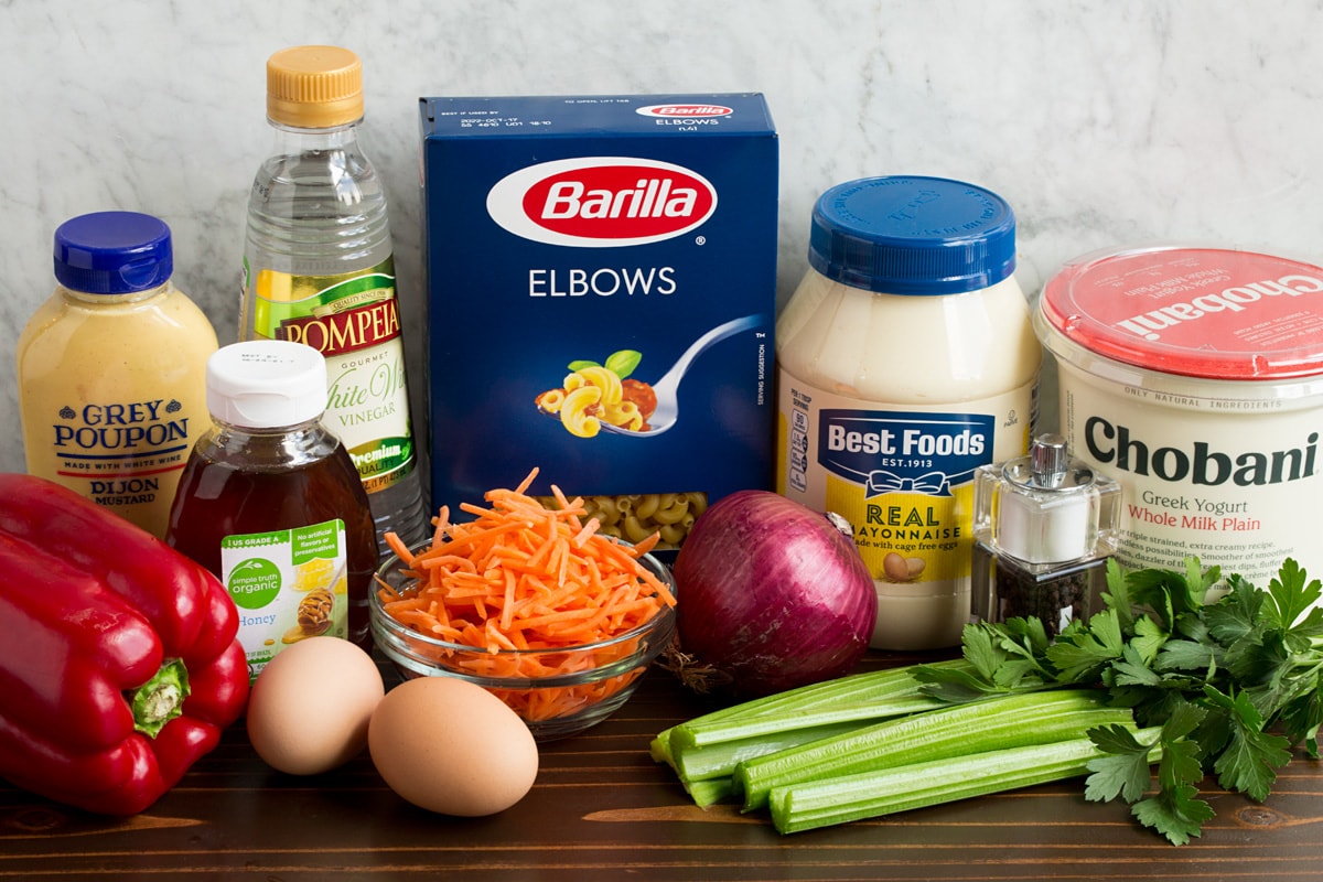 Macaroni Salad Ingredients that are in macaroni salad shown here. Includes mayonnaise, Greek yogurt, dijon mustard, honey, eggs, carrots, bell pepper, celery, parsley, vinegar, salt and pepper.