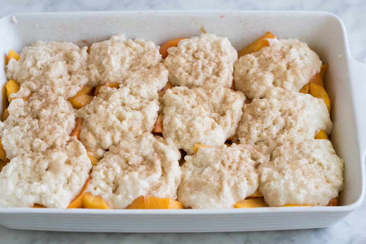 Peach Cobbler - the only peach cobbler recipe you'll ever need! I've never found better! Light and fluffy, buttery topping and perfectly sweet and juicy peach filling. #peach #cobbler #dessert #recipe Prepared cobbler with cinnamon sugar topping, shown before baking in oven.