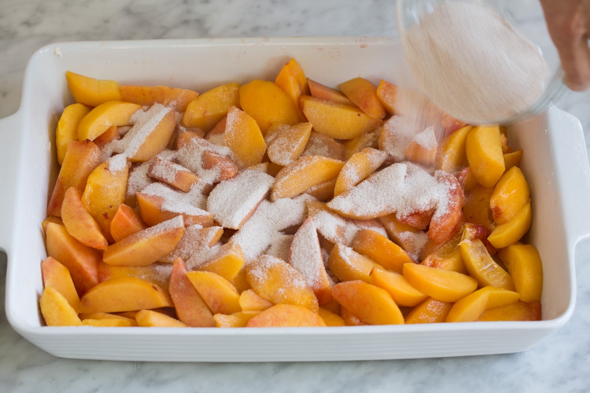 Peach Cobbler - the only peach cobbler recipe you'll ever need! I've never found better! Light and fluffy, buttery topping and perfectly sweet and juicy peach filling. #peach #cobbler #dessert #recipe Pouring sugar mixture over peaches in baking dish.