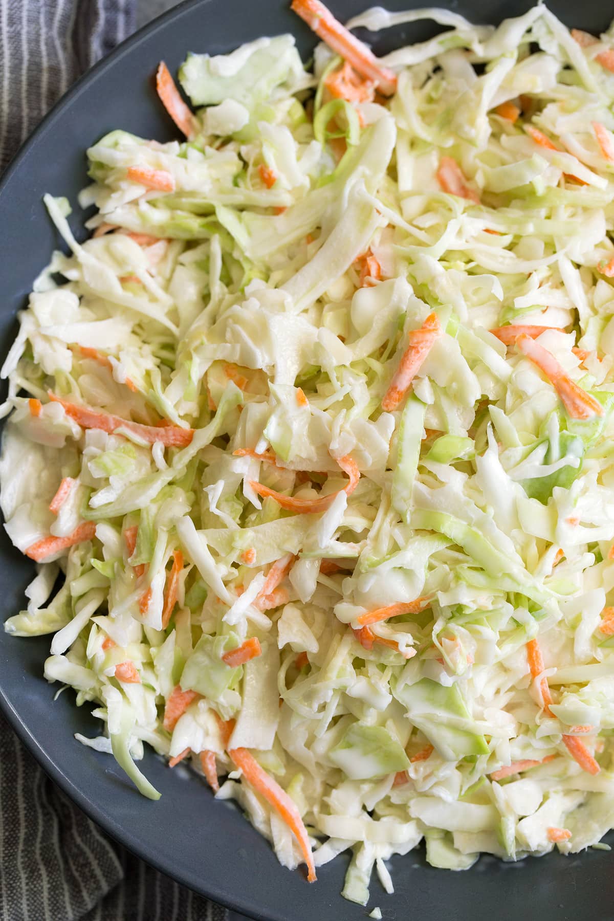 Coleslaw Recipe Close up image of coleslaw with dressing in a dark blue bowl.