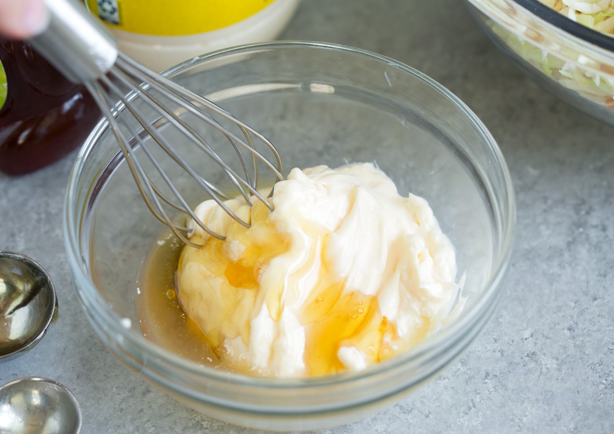 Coleslaw Recipe Making coleslaw dressing in mixing bowl with 3 ingredients including mayonnaise, honey, apple cider vinegar.