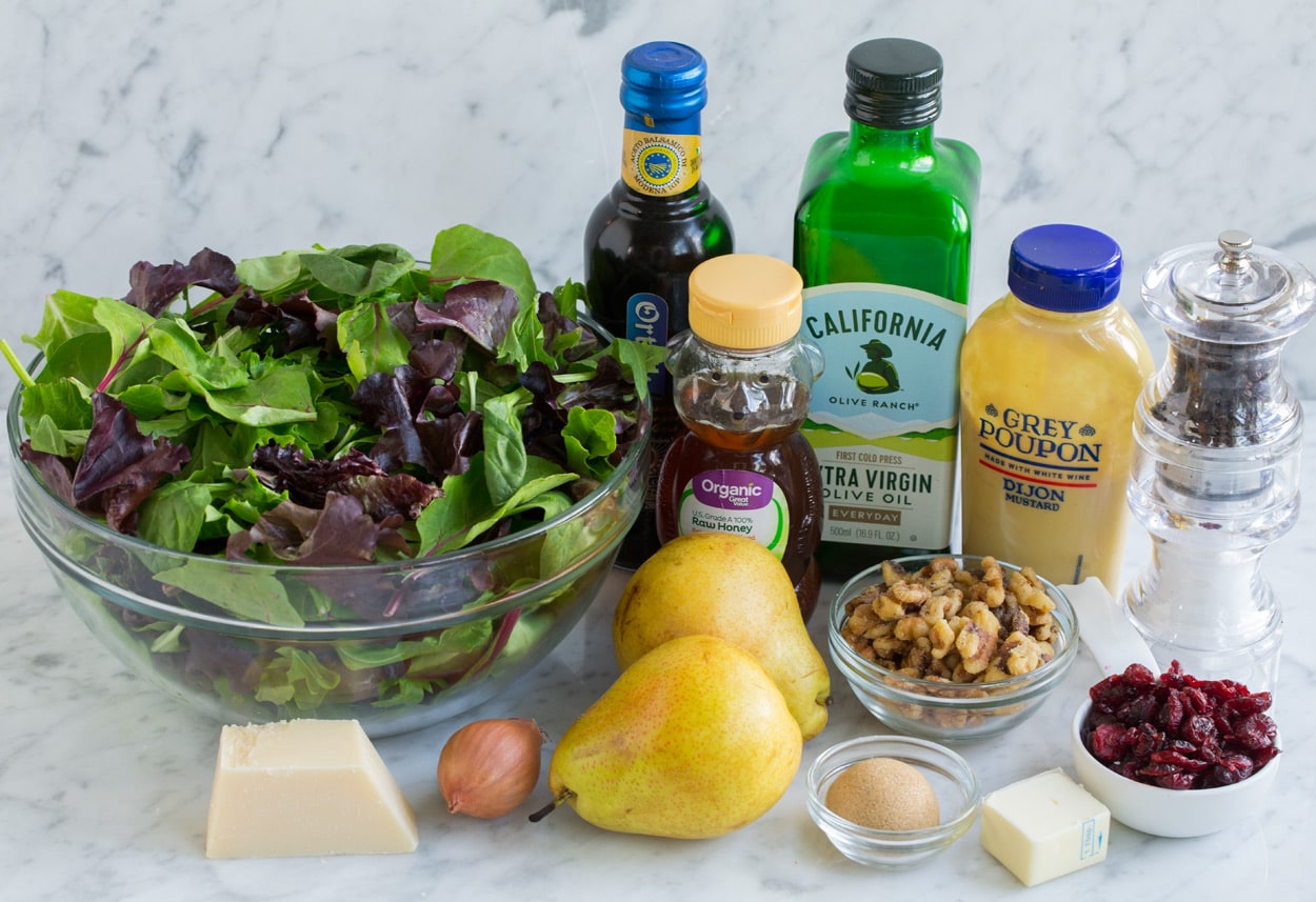 Pear Salad Ingredients for pear salad sitting on marble surface. Includes spring greens, pears, parmesan, olive oil, balsamic vinegar, butter, pecans, cranberries, mustard, honey, brown sugar.