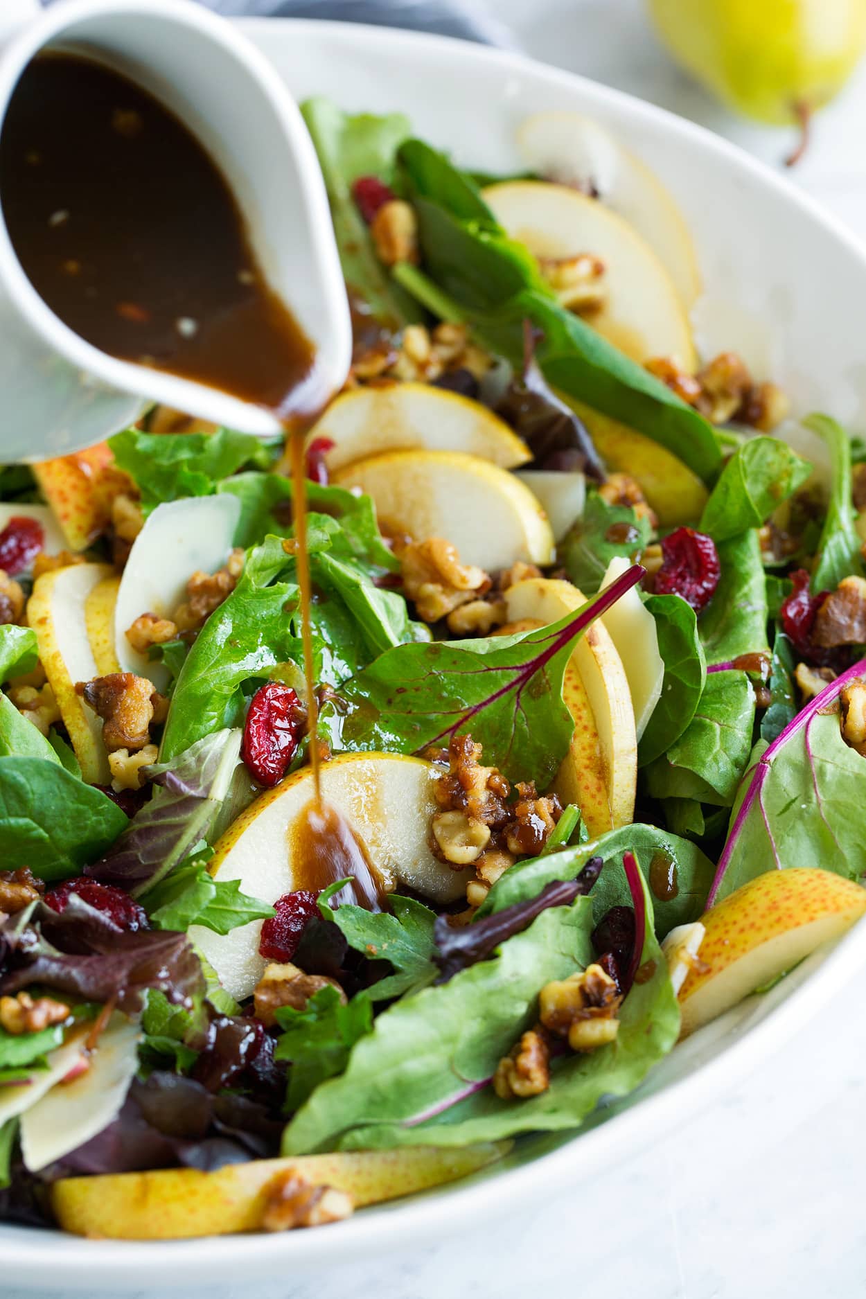 Pear Salad Pouring Balsamic Vinaigrette over Pear Salad in Salad Bowl