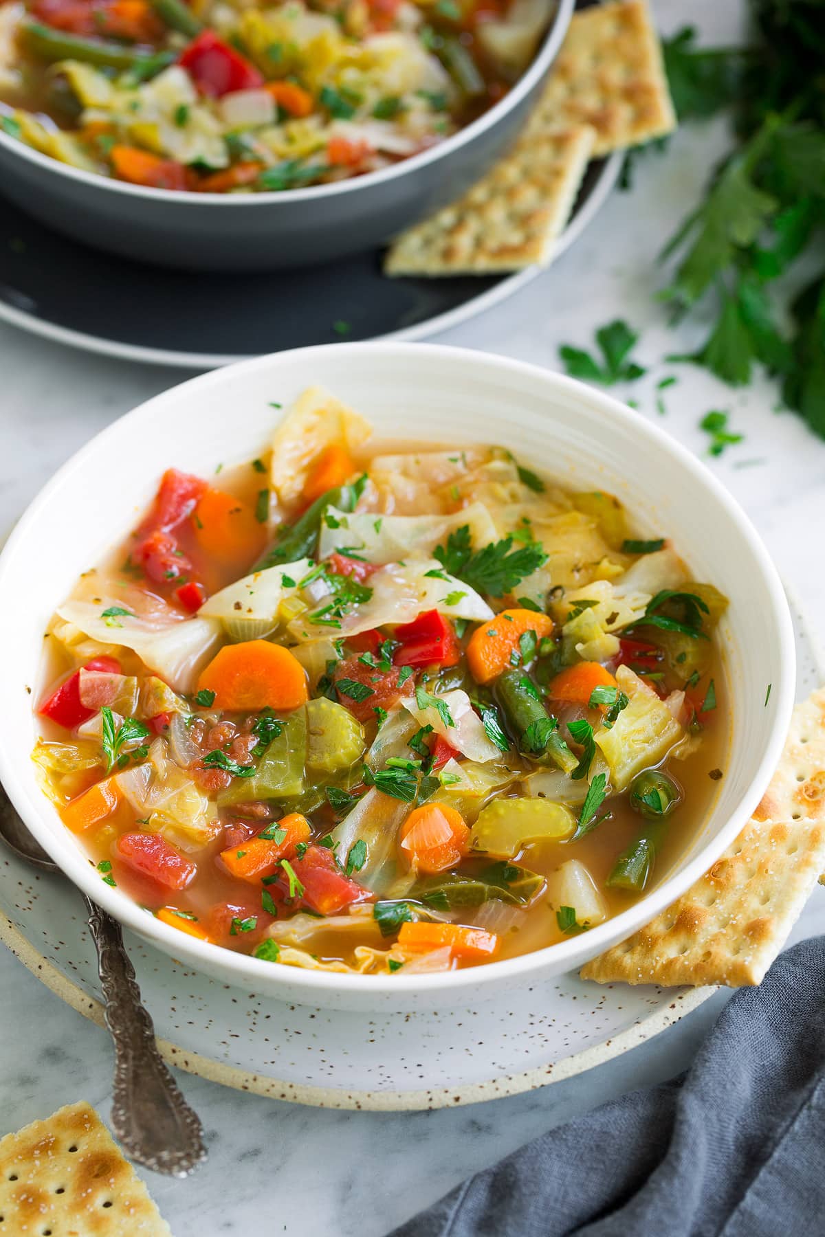 Cabbage Soup Single serving of easy homemade cabbage soup in a white bowl set over a white speckled plate with crackers to the side.