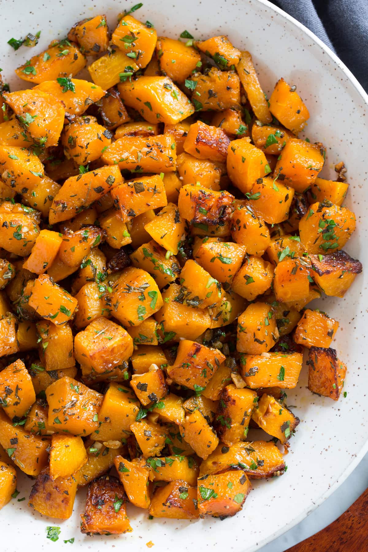 Roasted Butternut Squash with Garlic and Herbs Roasted Butternut Squash in a white ceramic serving bowl set over a white marble surface.