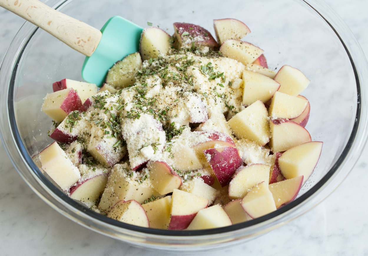 Garlic Parmesan and Herb Roasted Potatoes Showing how to roast potatoes. Tossing potato chunks in a bowl with oil, garlic and herbs.