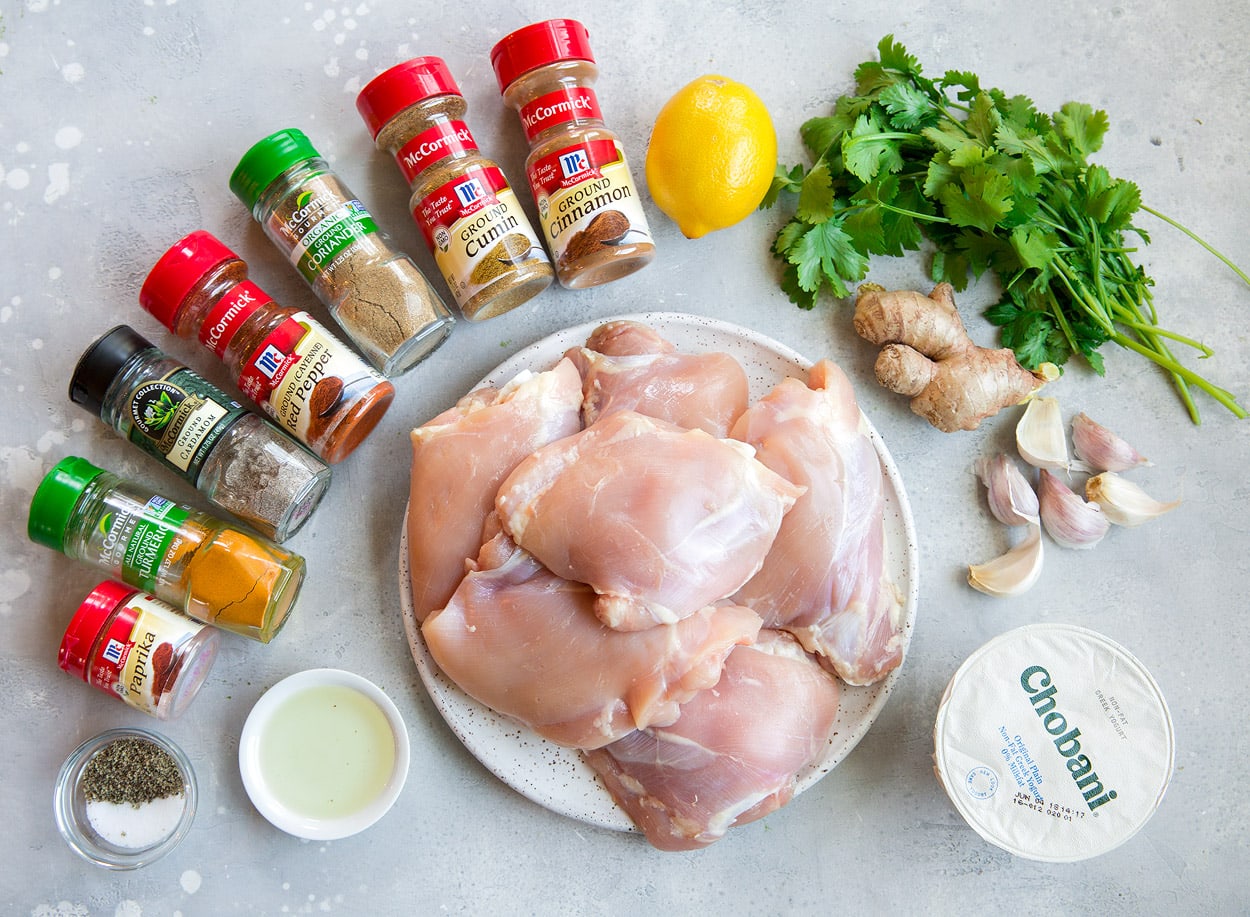 Tandoori Chicken Tandoori Chicken Ingredients including spices, chicken thighs, oil, lemon, cilantro, garlic and greek yogurt shown here on a grey surface.