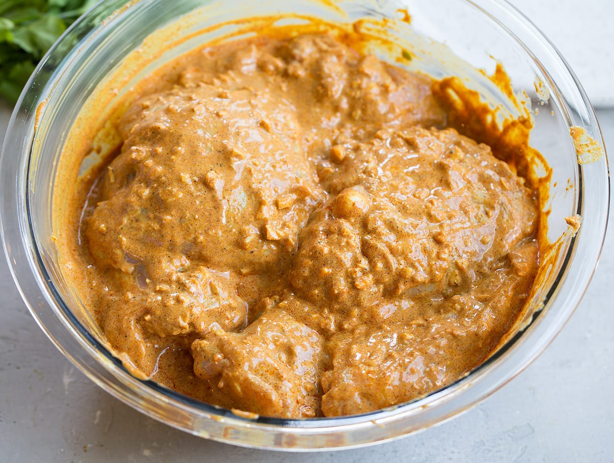 Tandoori Chicken Tossing chicken with marinade in glass mixing bowl to make Tandoori Chicken.