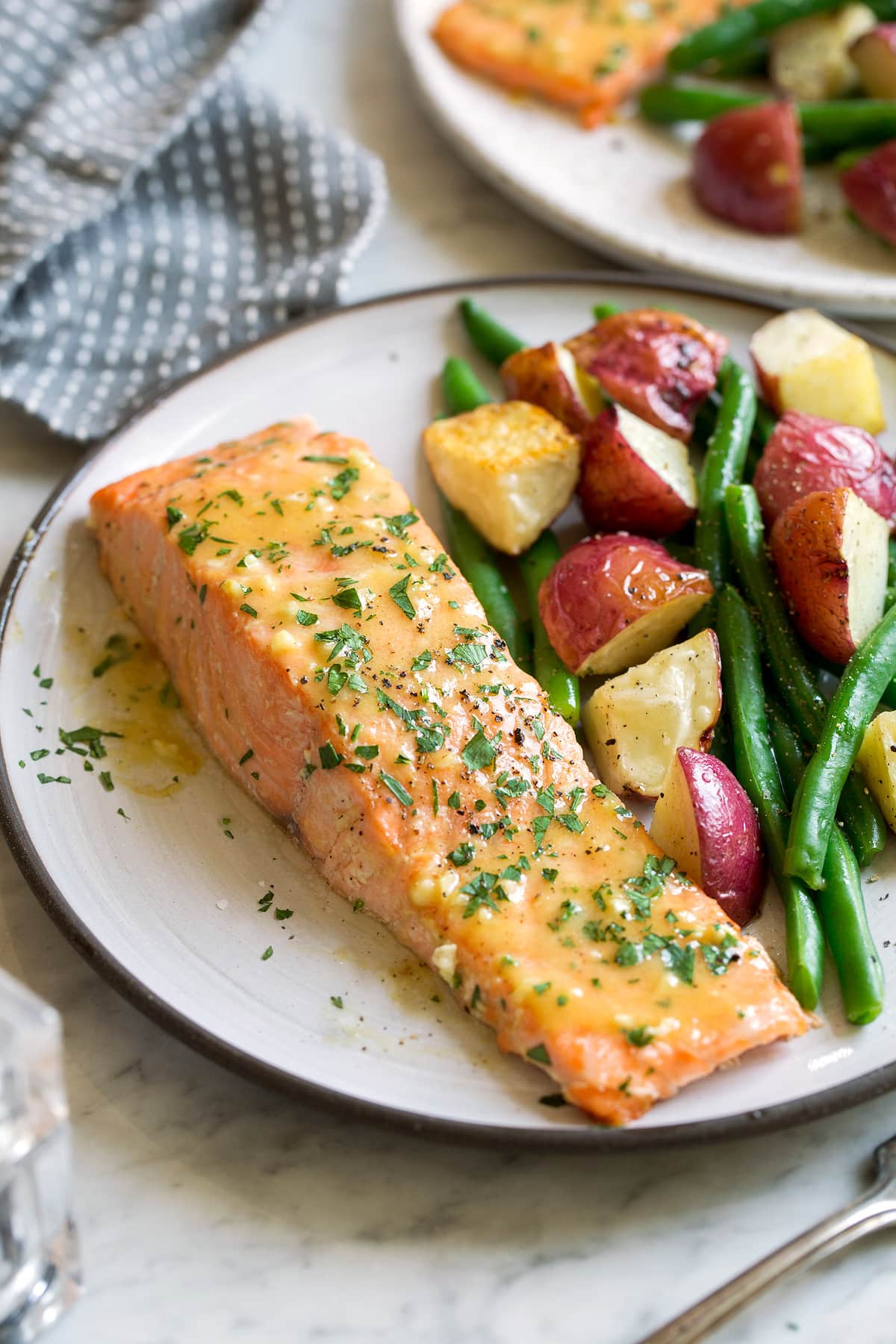 Baked Salmon with Buttery Honey Mustard Sauce Single baked salmon fillet on a serving dish with a side of roasted potatoes and carrots. Salmon is brushed with a honey mustard sauce.