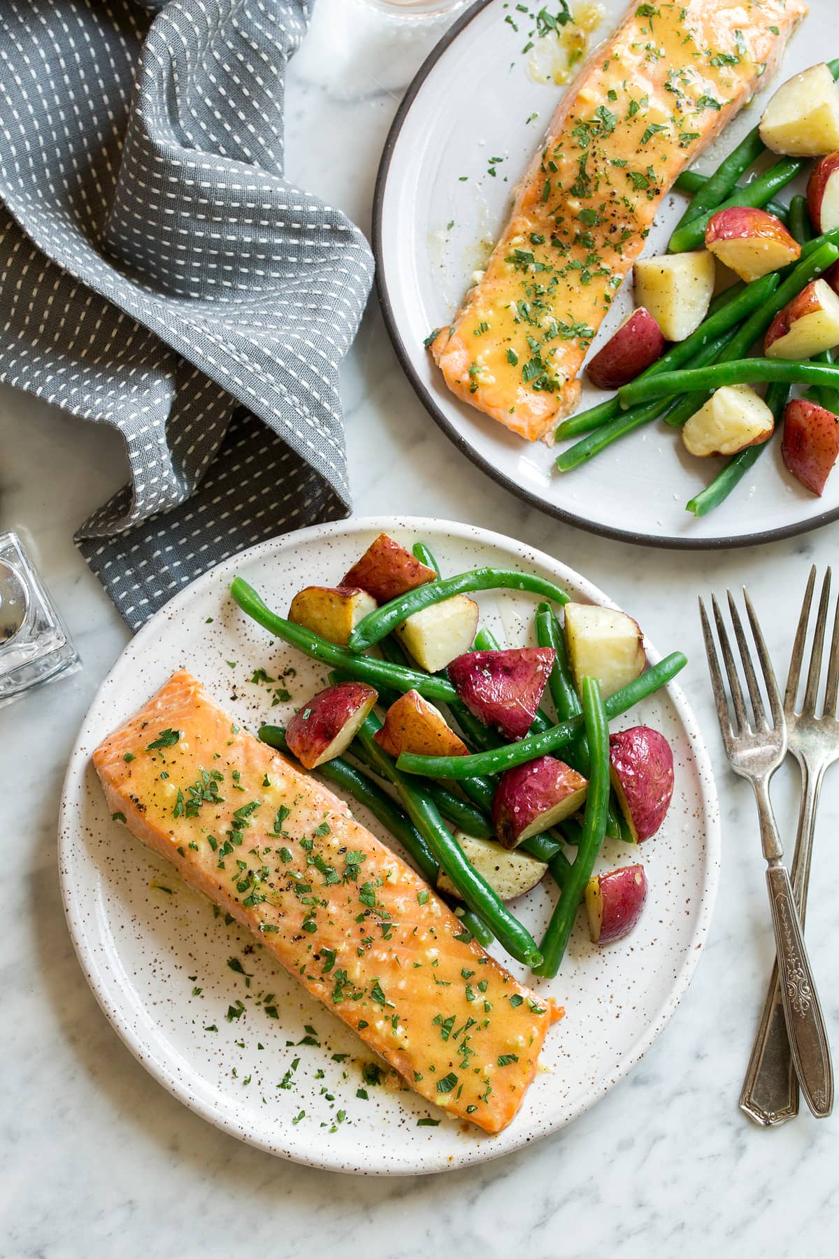 Baked Salmon with Buttery Honey Mustard Sauce Overhead image of two servings of Baked Salmon with Buttery Honey Mustard Sauce on white serving plates set over a marble surface.