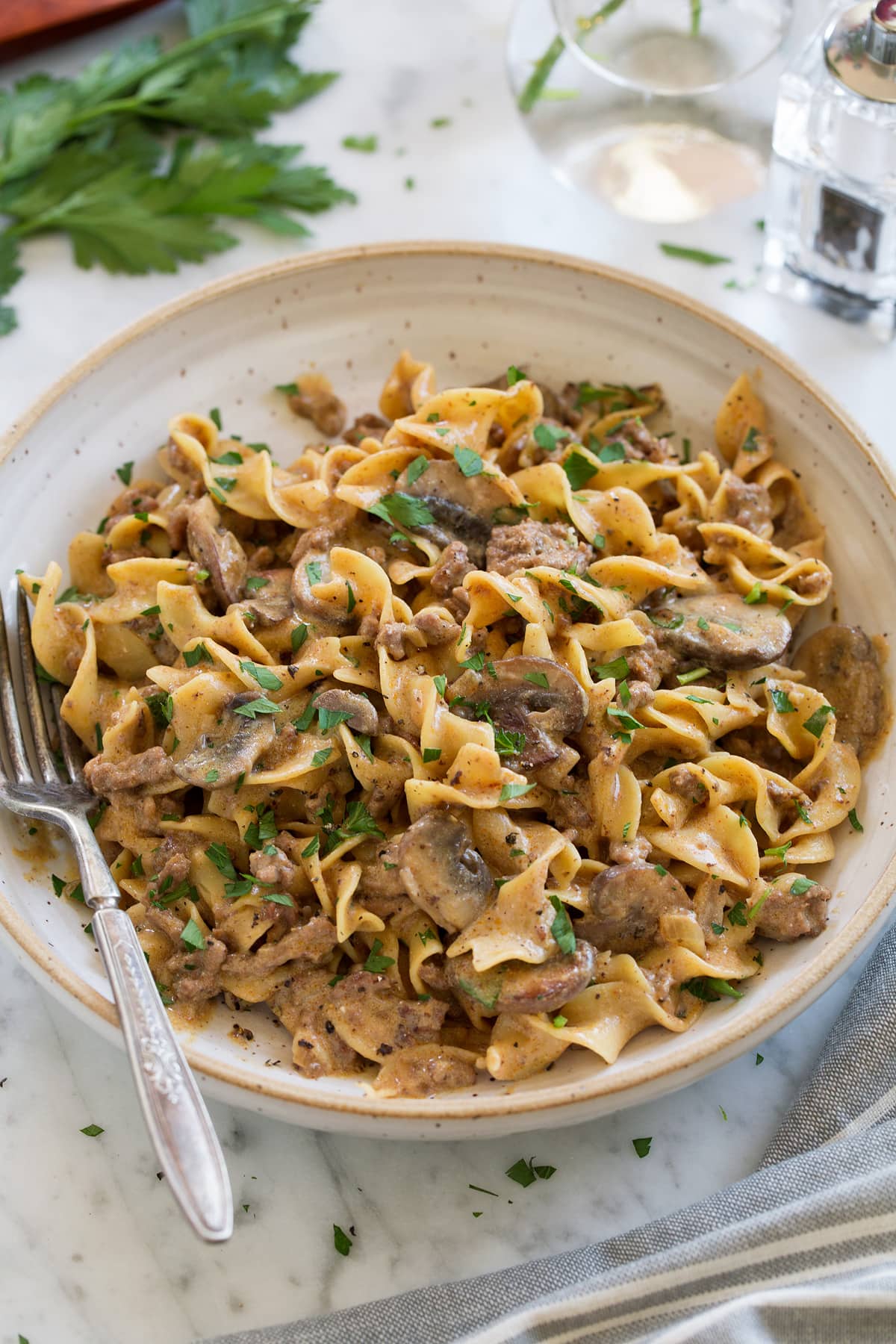 Beef Stroganoff One Pot Easy Beef Stroganoff shown in a cream pasta bowl with a fork to the side. Bowl is sitting on a marble surface, parsley and a salt shaker are in the background.