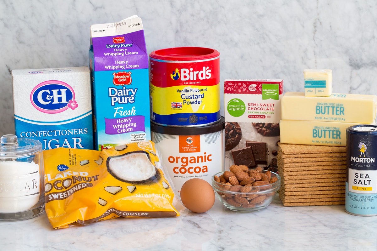 Nanaimo Bars Image of ingredients used to make Nanaimo Bars. Includes sugar, coconut, powdered sugar, cream, custard powder, cocoa powder, egg, almonds, chocolate, graham crackers, butter, and salt.