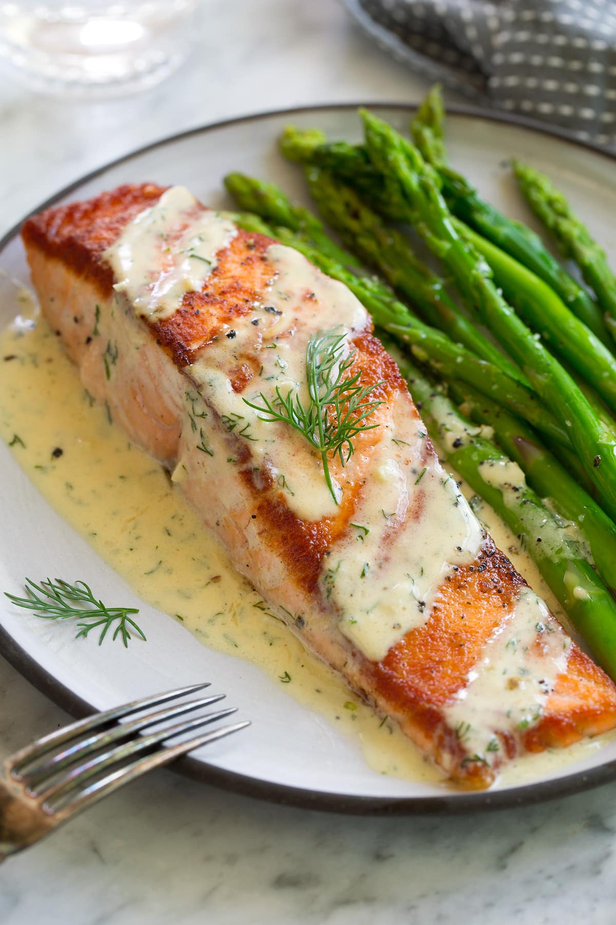 Salmon with Creamy Garlic Dijon Sauce A single pan seared salmon fillet on a white plate. Salmon is drizzled with a creamy mustard sauce and sprinkled with dill. It's served with a side of asparagus.
