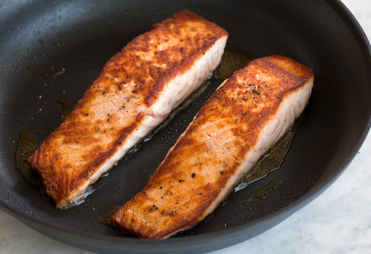 Salmon with Creamy Garlic Dijon Sauce Two golden brown pan seared salmon fillets shown here in large non-stick skillet.