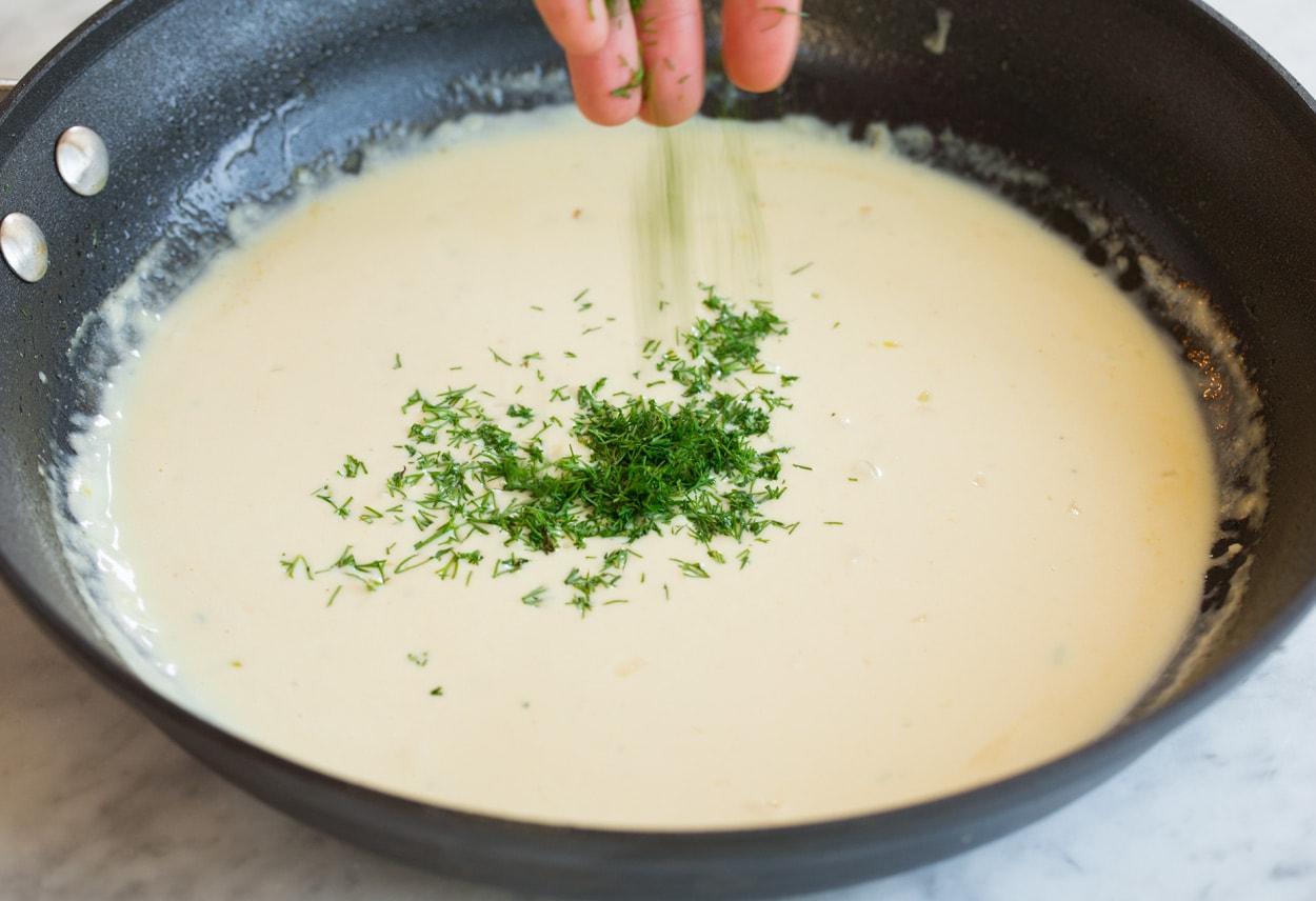 Salmon with Creamy Garlic Dijon Sauce Adding dill to sauce in skillet for pan seared salmon.