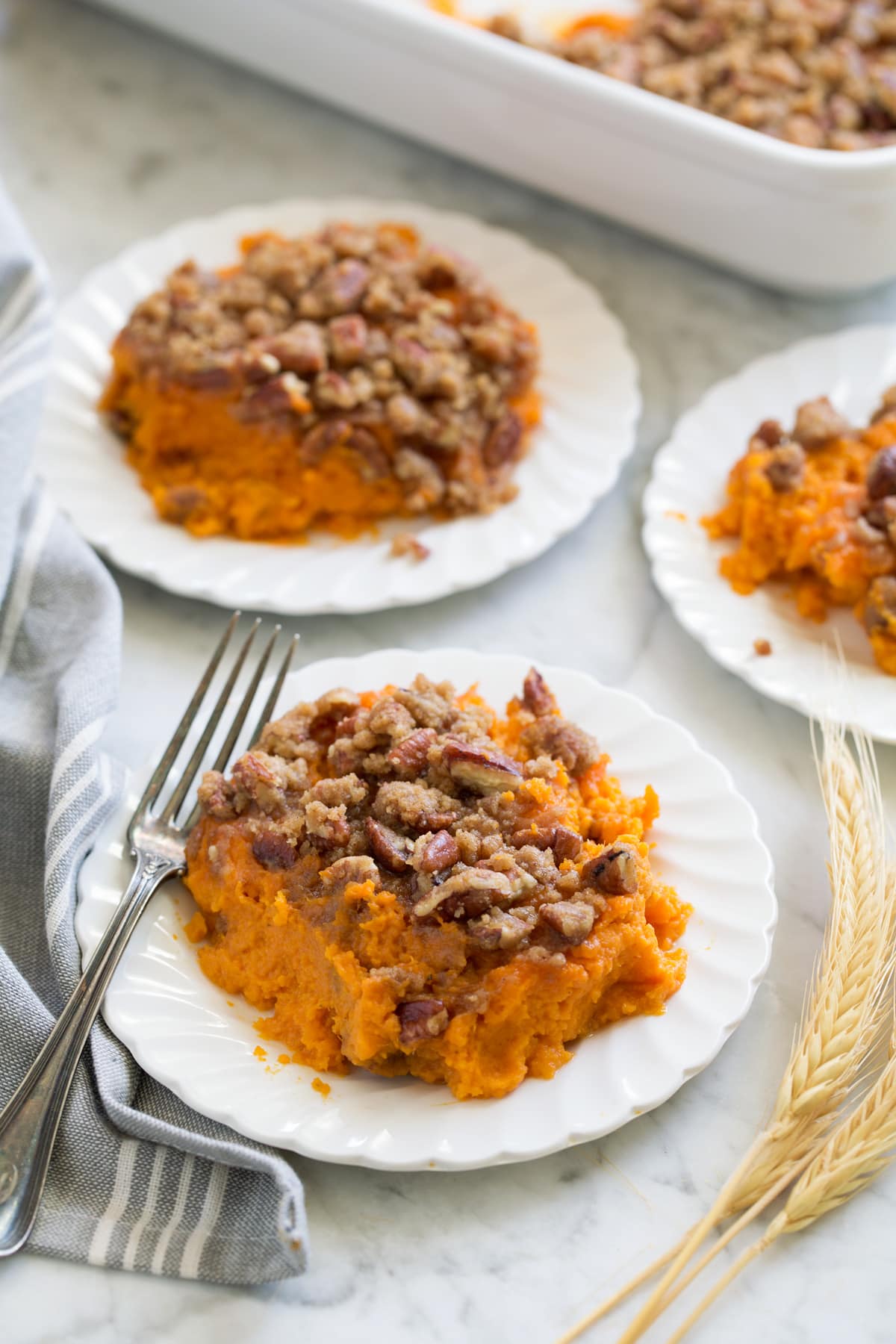 Sweet Potato Casserole Sweet Potato Casserole shown in three individual servings and small white scalloped plates set over a marble surface.