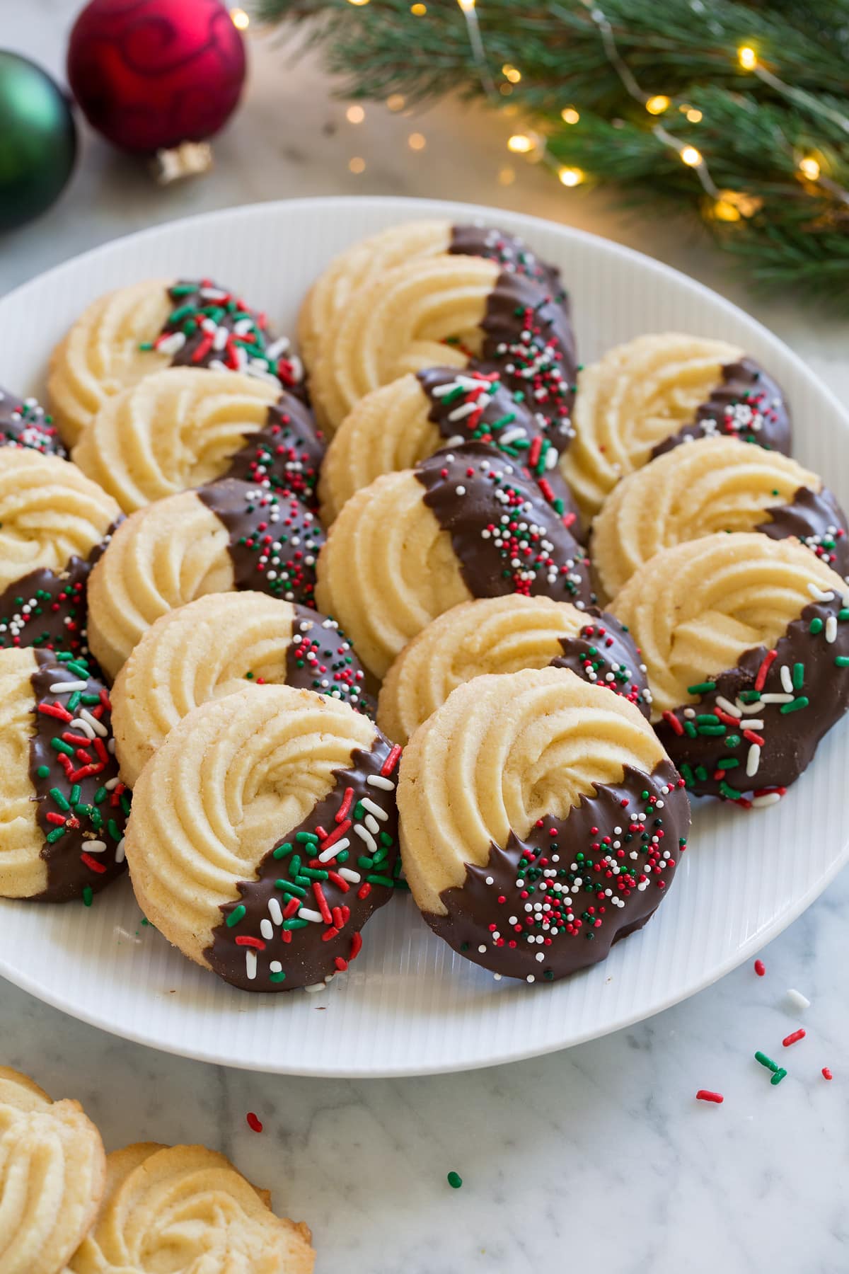 Butter Cookies Butter Cookies dipped in chocolate and covered in sprinkles. Shown in rows on a white serving plate.