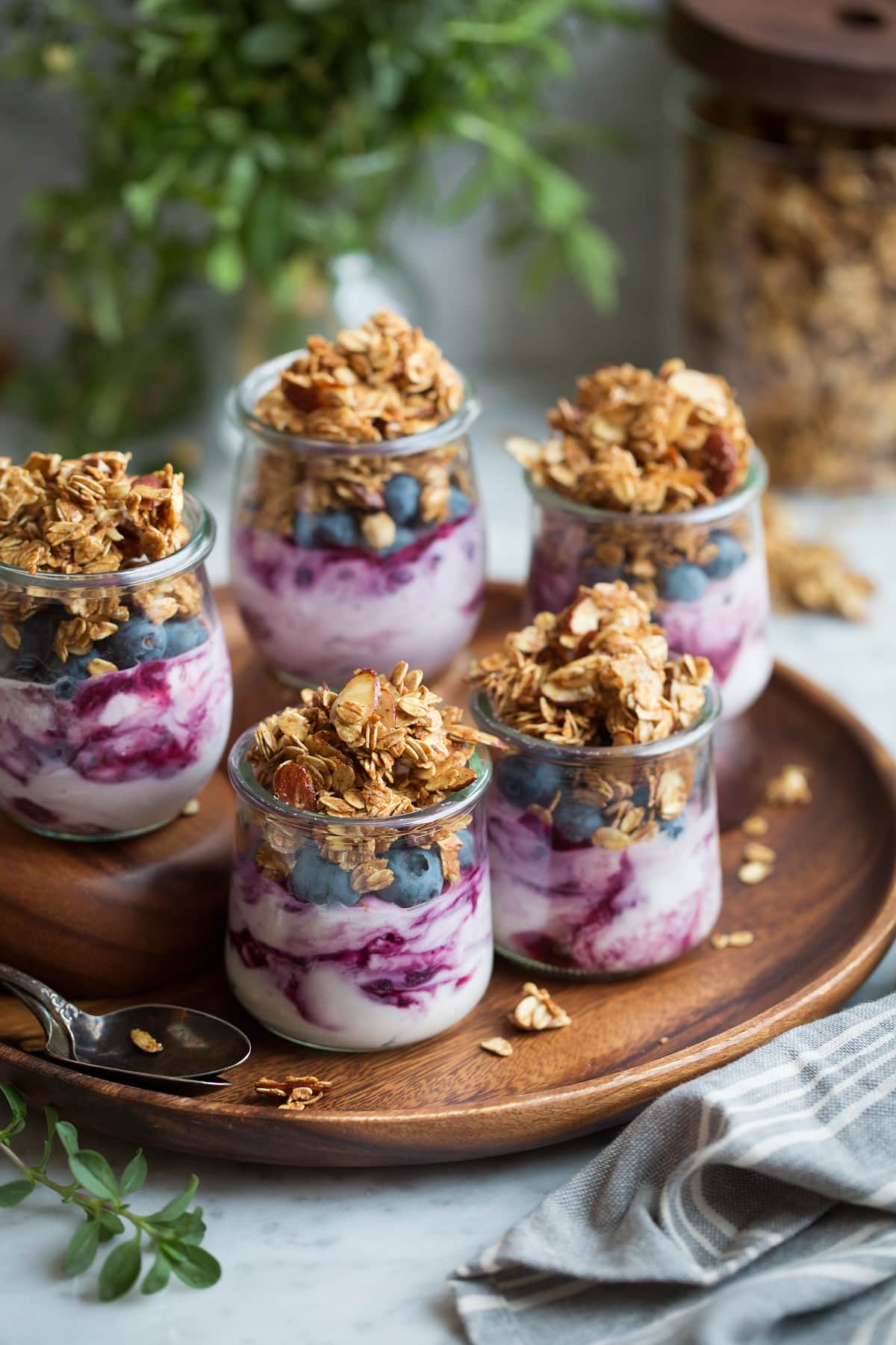 Homemade Granola Recipe Five servings of granola, yogurt and berries in glass jars.