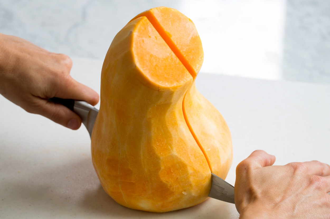Roasted Butternut Squash with Garlic and Herbs Showing how to halve a butternut squash on a cutting board.