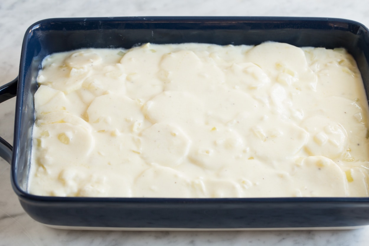 Scalloped Potatoes Finishing scalloped potatoes by adding a final layer of sauce over thinly sliced potatoes in baking dish.