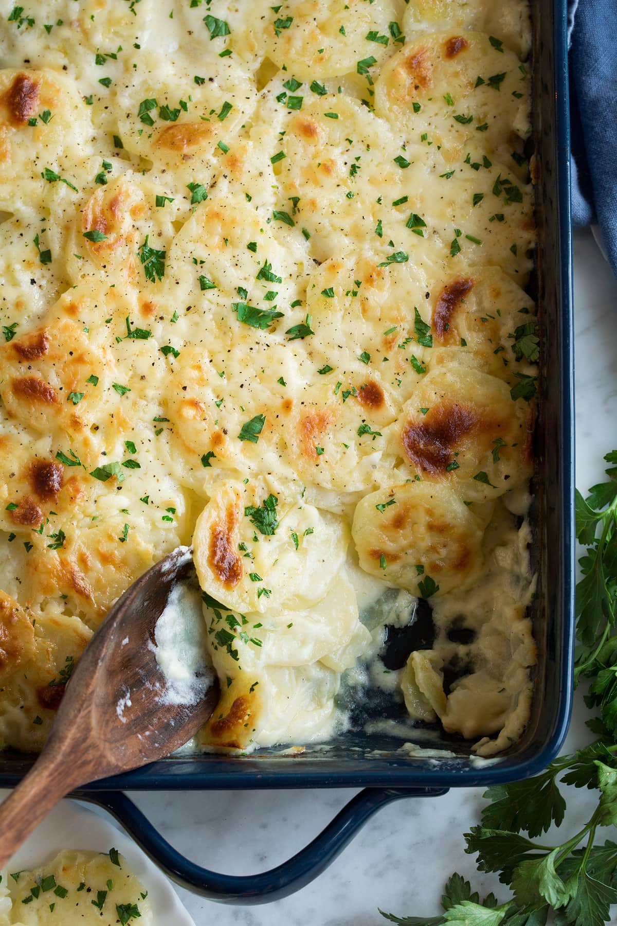 Scalloped Potatoes Scalloped Potatoes in a navy baking dish with one scoop removed to show creamy sauce and potato layers.