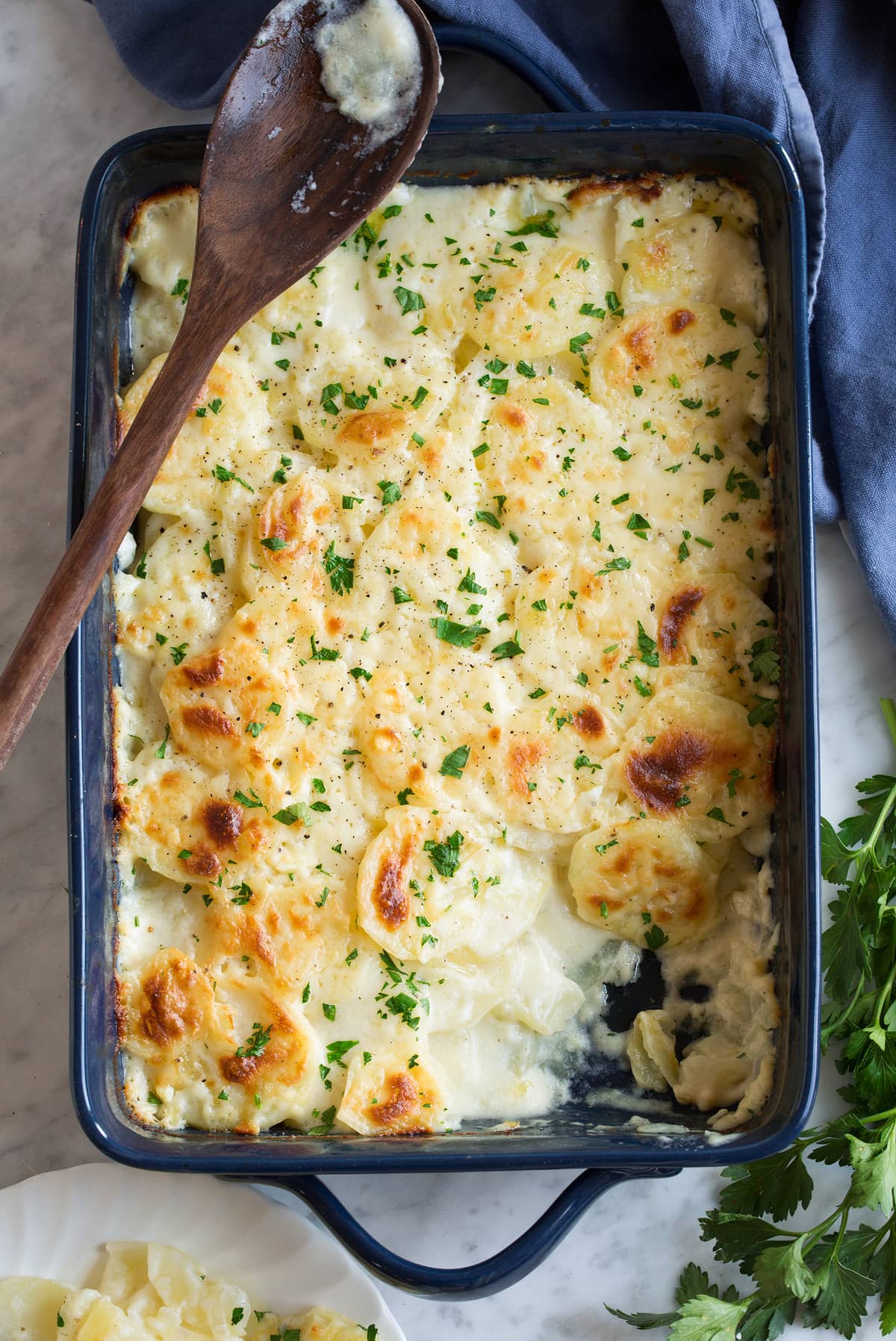 Scalloped Potatoes Scalloped Potatoes after baking in a dark baking dish set over marble surface. One scoop is removed to show sauce and thin sliced potatoes.