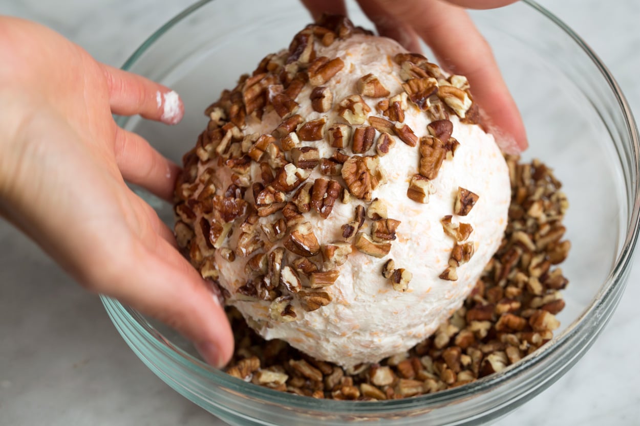 Cheese Ball Recipe Rolling cheese ball through chopped pecans in a mixing bowl.