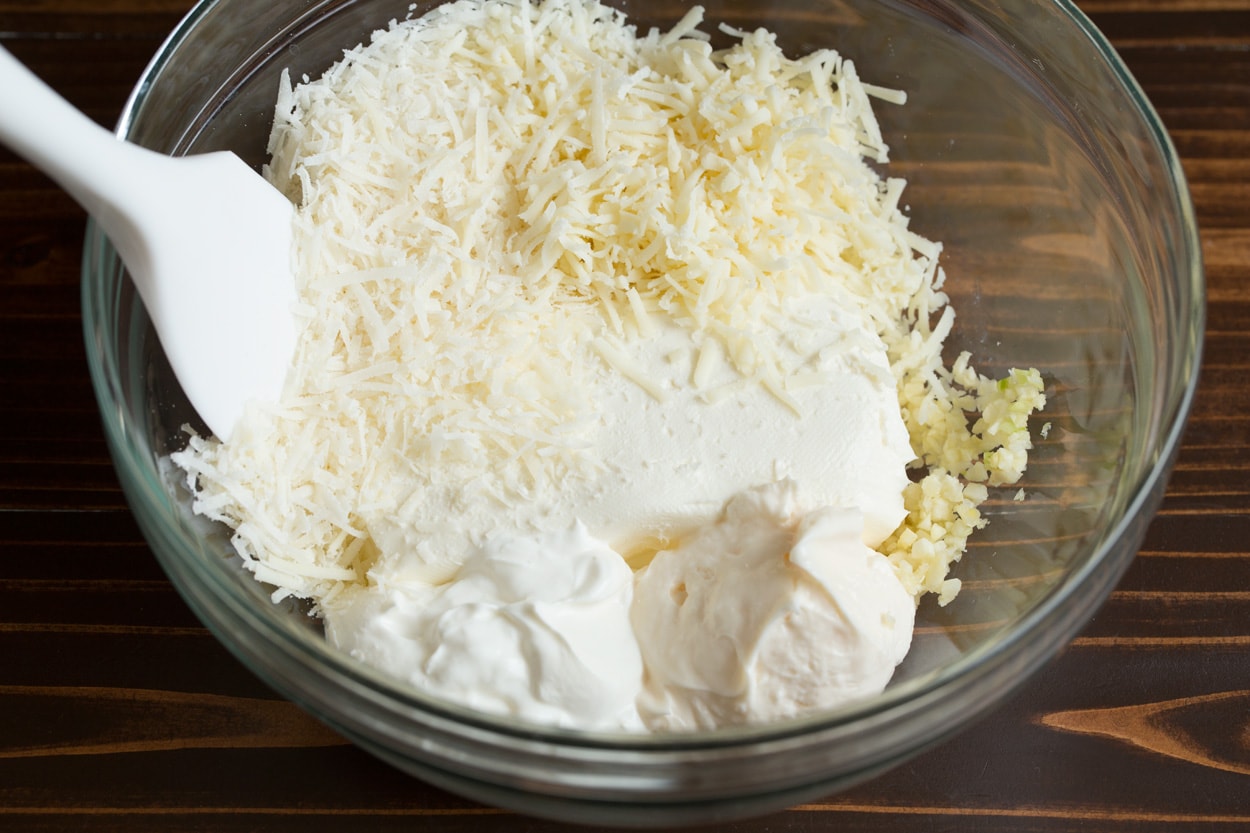Spinach Artichoke Dip Mixing cream cheese, mayonnaise, sour cream, garlic and shredded cheeses in mixing bowl to make Spinach Artichoke Dip.