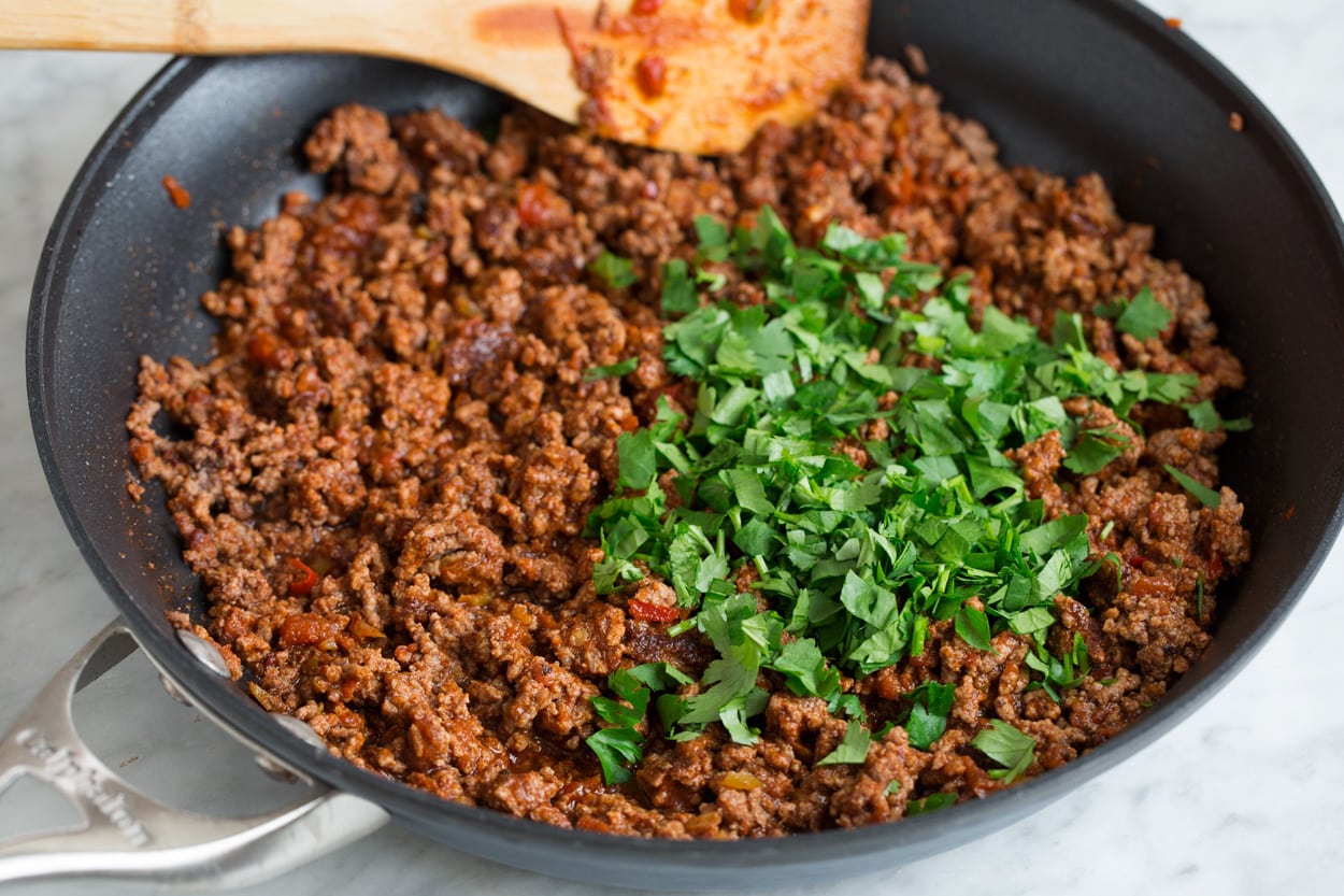 Taco Salad - so easy and flavorful! Adding cilantro to finished taco salad beef mixture in skillet.