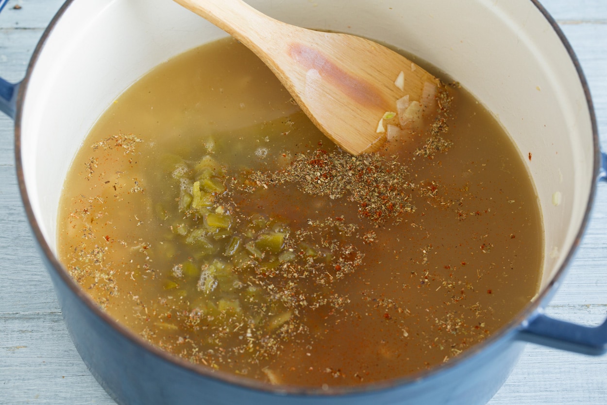 White Chicken Chili Adding broth, spices and green chilis to white chicken chili mixture in pot.