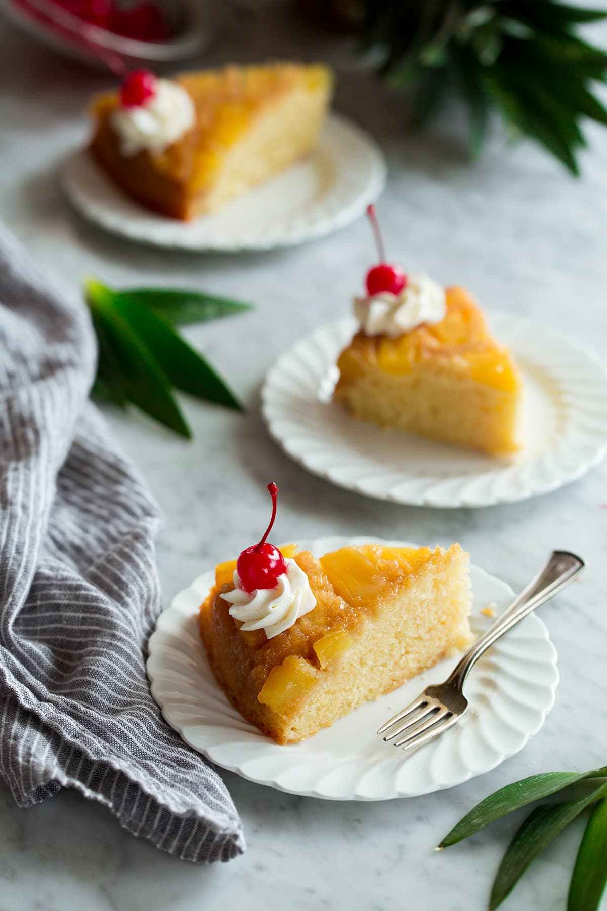 Pineapple Upside Down Cake Three slices of Pineapple Upside Down Cake on individual white ruffled dessert plates.