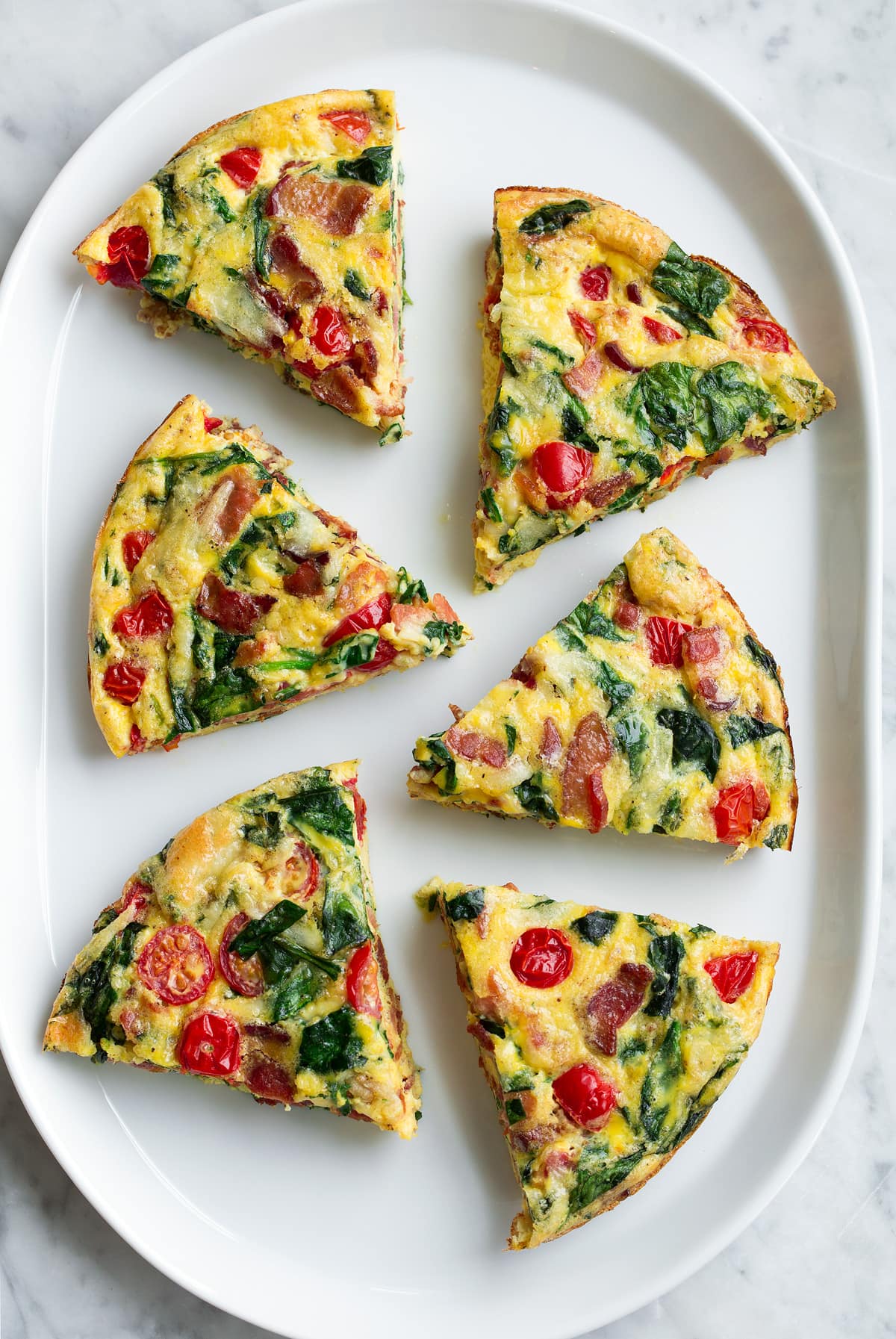 Frittata Recipe (Bacon, Spinach, Tomato and Swiss) Overhead image of six frittata wedges on a white serving platter.
