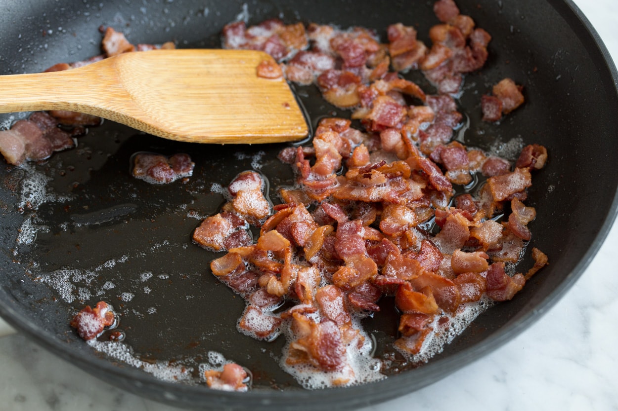 Frittata Recipe (Bacon, Spinach, Tomato and Swiss) Sauteeing bacon in a large black skillet to make a frittata.