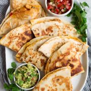 Overhead image of 8 quesadilla wedges on a white oblong platter served with pico and guacamole.