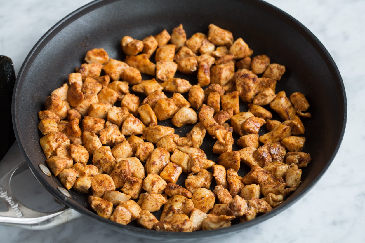 Loaded Quesadillas Sautéing spiced chicken cubes in a large black skillet for quesadillas.