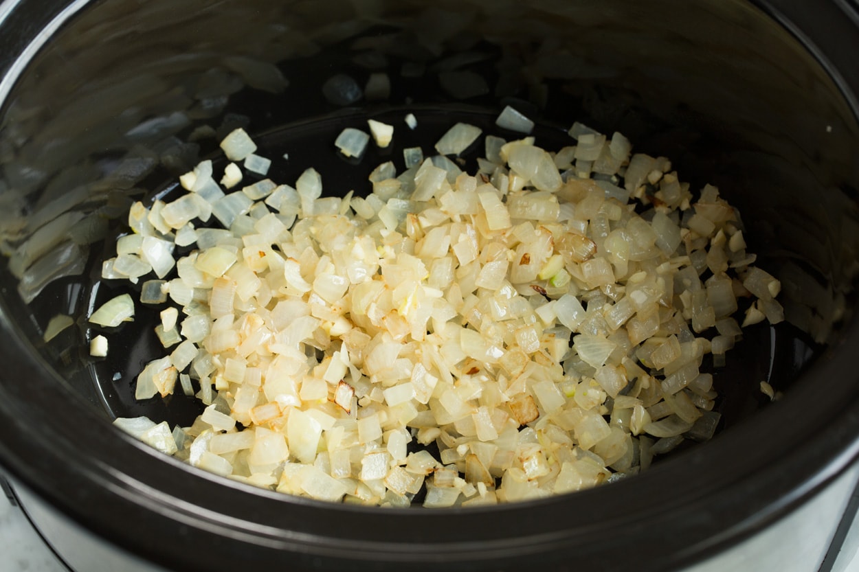 Showing the steps to making chili. Adding sautéed onions to crockpot for chili.