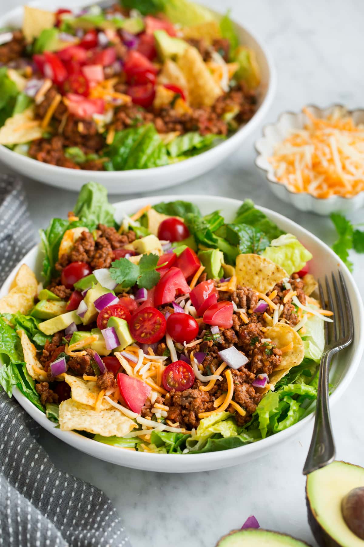 Taco Salad - so easy and flavorful! Two servings of taco salad in white bowls set over a marble table.