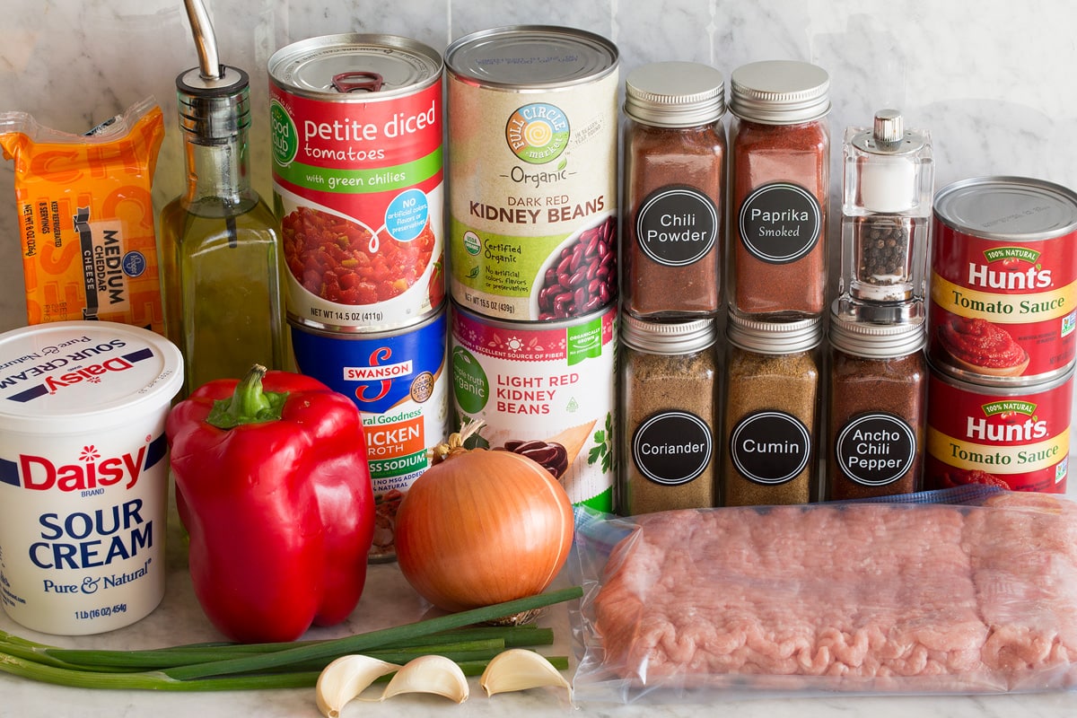 Turkey Chili Photo of ingredients used to make turkey chili. Includes ground turkey, tomato sauce, chili powder, ancho chili powder, smoked paprika, cumin, coriander, light and dark red kidney beans, chicken broth, canned tomatoes, bell pepper, yellow onion, green onions, garlic, olive oil, sour cream, and cheddar cheese.