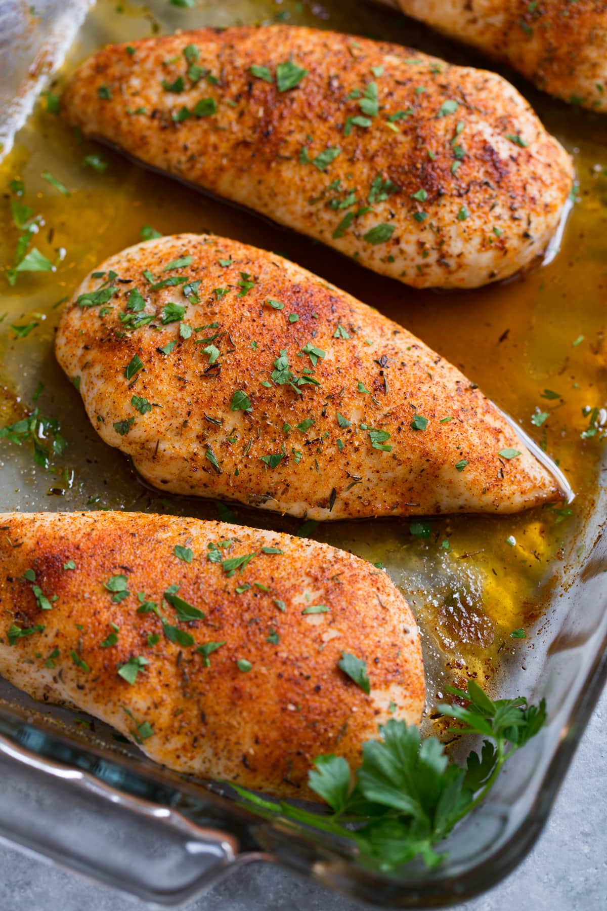 Baked Chicken Breasts Close up image of chicken breast in glass baking dish set over a grey surface, after baking in the oven.