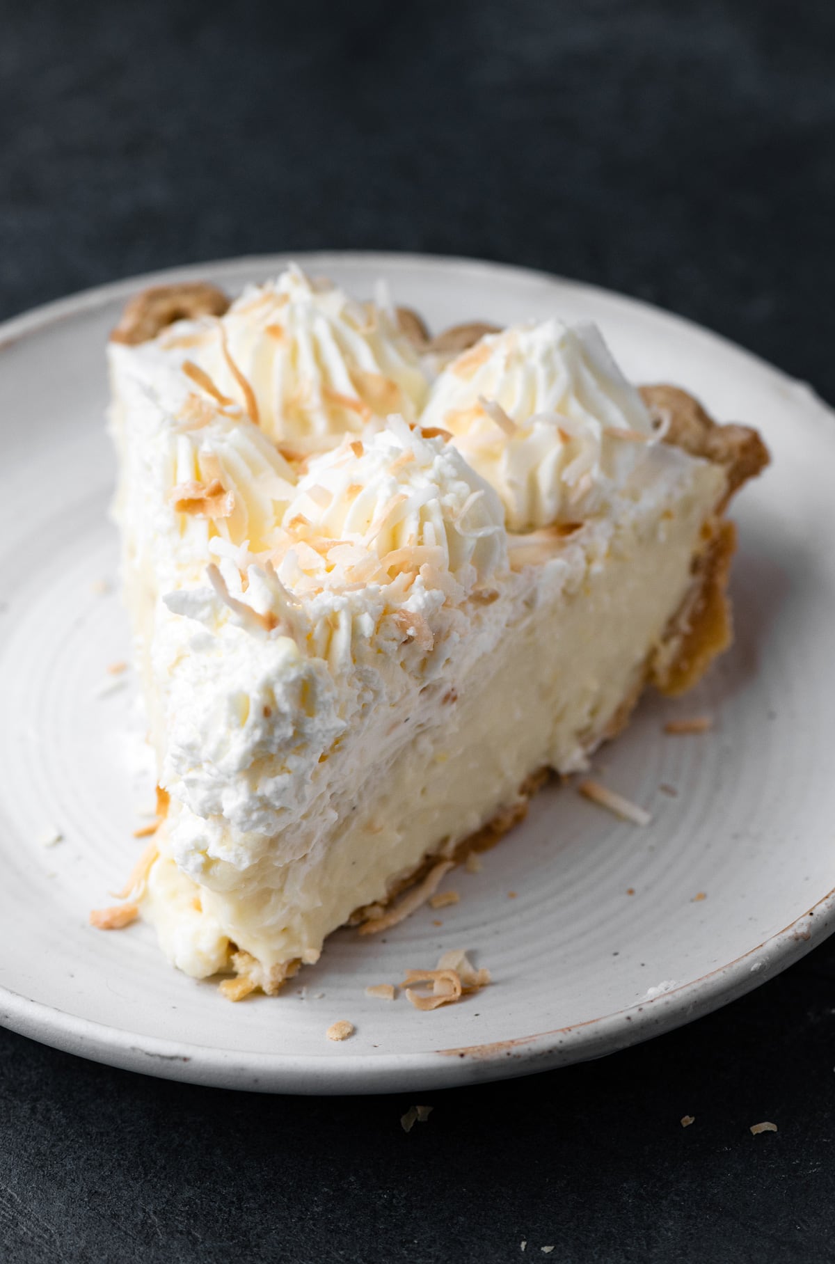 Coconut Cream Pie Single slice of coconut cream pie made from scratch on a white dessert plate.