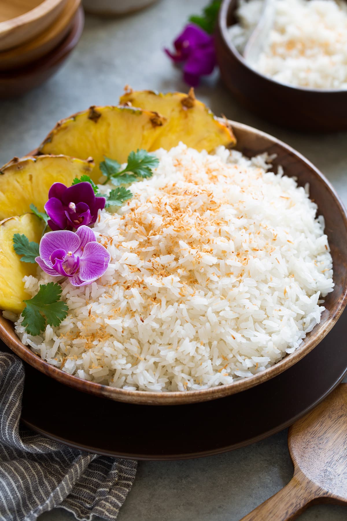 Coconut Rice Coconut rice in a wooden bowl set over a brown plate on a grey surface.