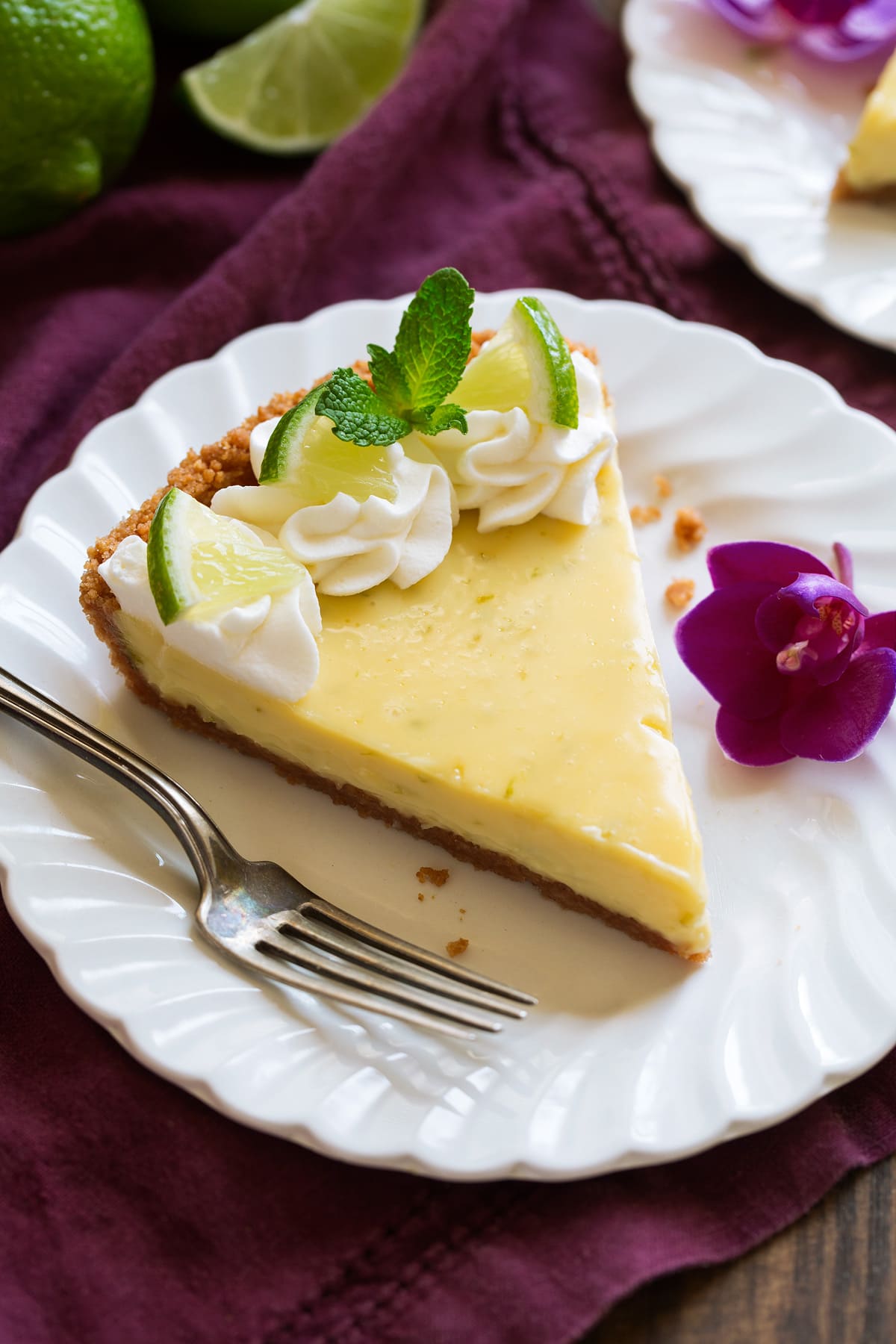 Best Ever Key Lime Pie! Slice of Best Key Lime Pie on white scalloped dessert plate set over a maroon napkin.