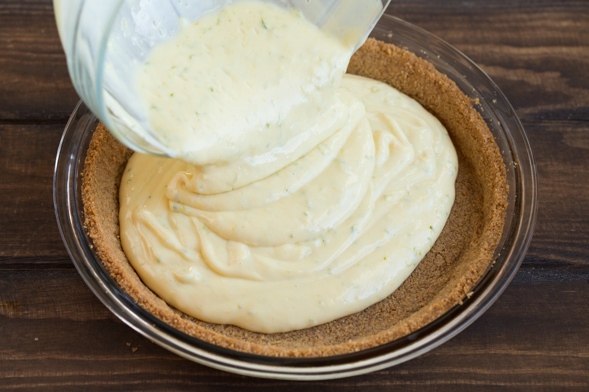 BEST EVER Key Lime Pie recipe! Pouring key lime pie filling over crust in glass pie pan.