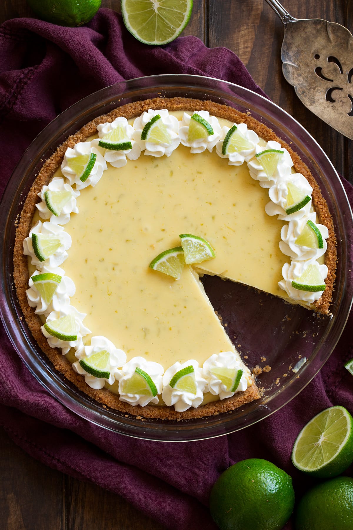 Best Ever Key Lime Pie! Whole key lime pie with one slice removed. Pie is decorated with swirls of whipped cream around the edges and mini lime slices.