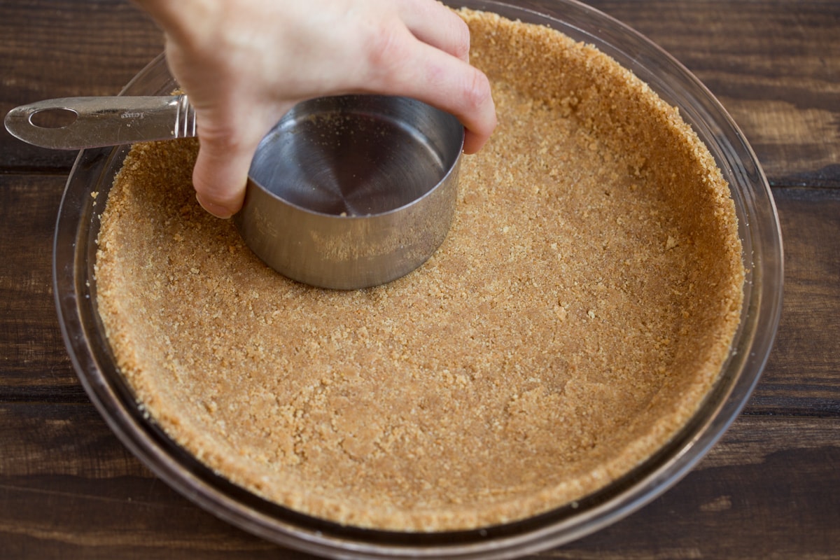 BEST EVER Key Lime Pie recipe! Pressing graham cracker crumbs into a 9-inch glass pie dish for key lime pie base.