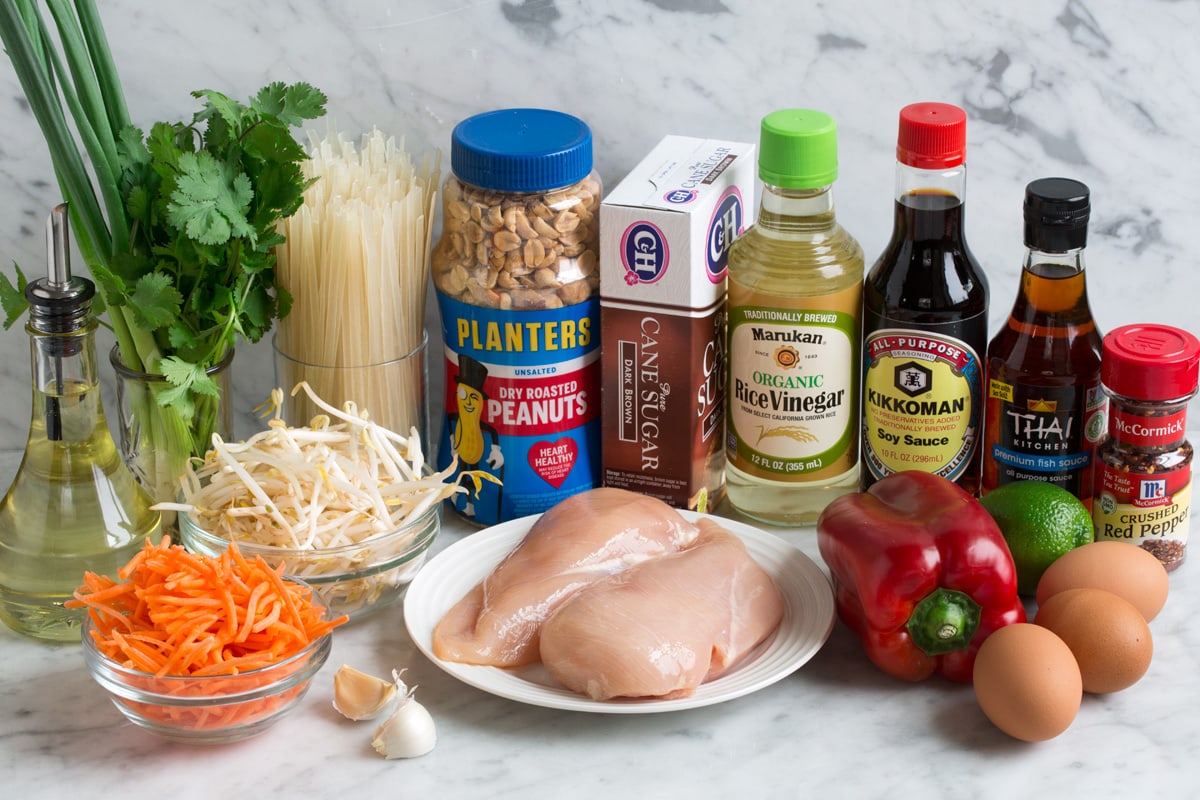 Pad Thai (with Chicken or Shrimp) Ingredients needed for pad thai shown here including eggs, red pepper flakes, fish sauce, soy sauce, rice vinegar, lime, bell pepper, chicken, brown sugar, peanuts, rice noodles, cilantro, green onions, bean sprouts, carrots, garlic and vegetable oil.