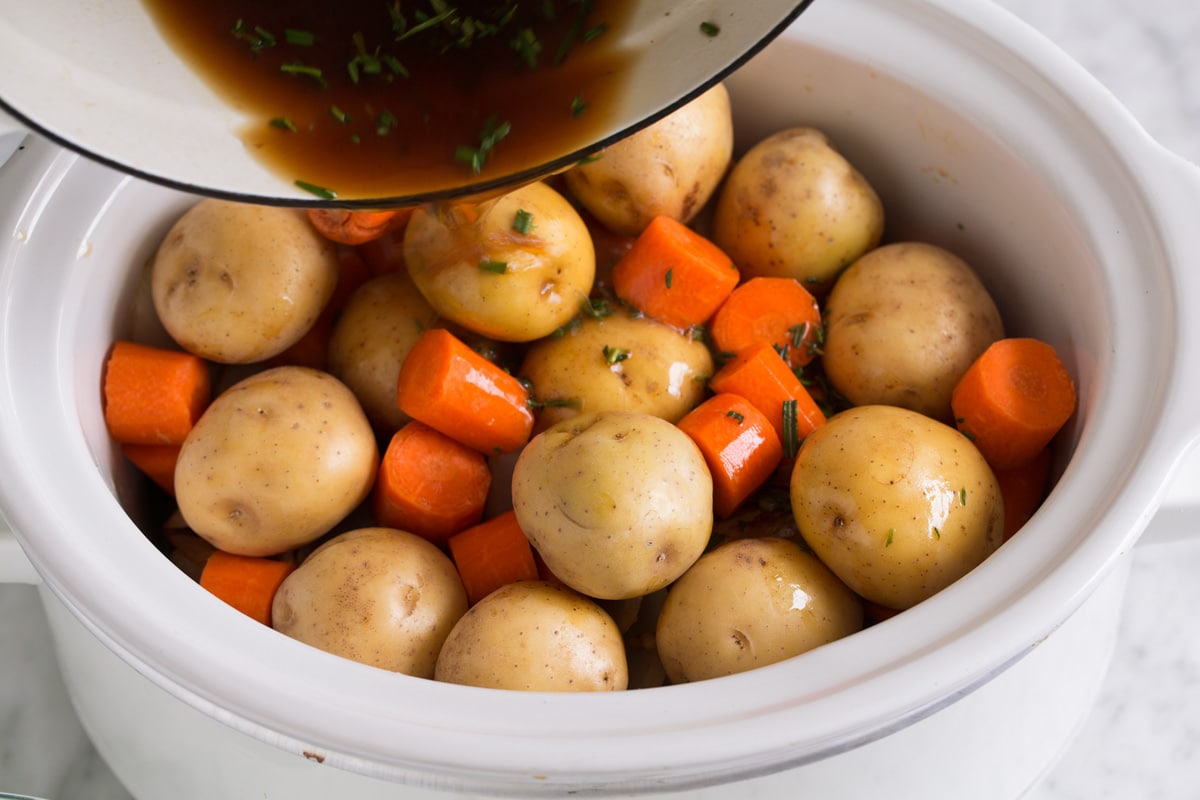 Ultimate Slow Cooker Pot Roast Adding potatoes and carrots over chuck roast and pouring over beef broth mixture.